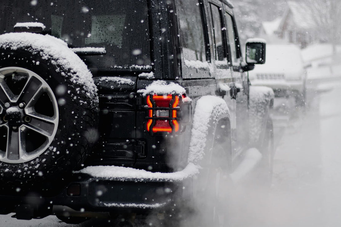 Black SUV driving on snowy road with visible snow on tires and tail light glow.