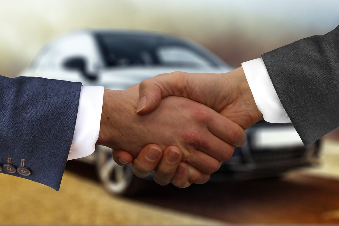 Business handshake in front of a car, symbolizing a vehicle purchase deal.