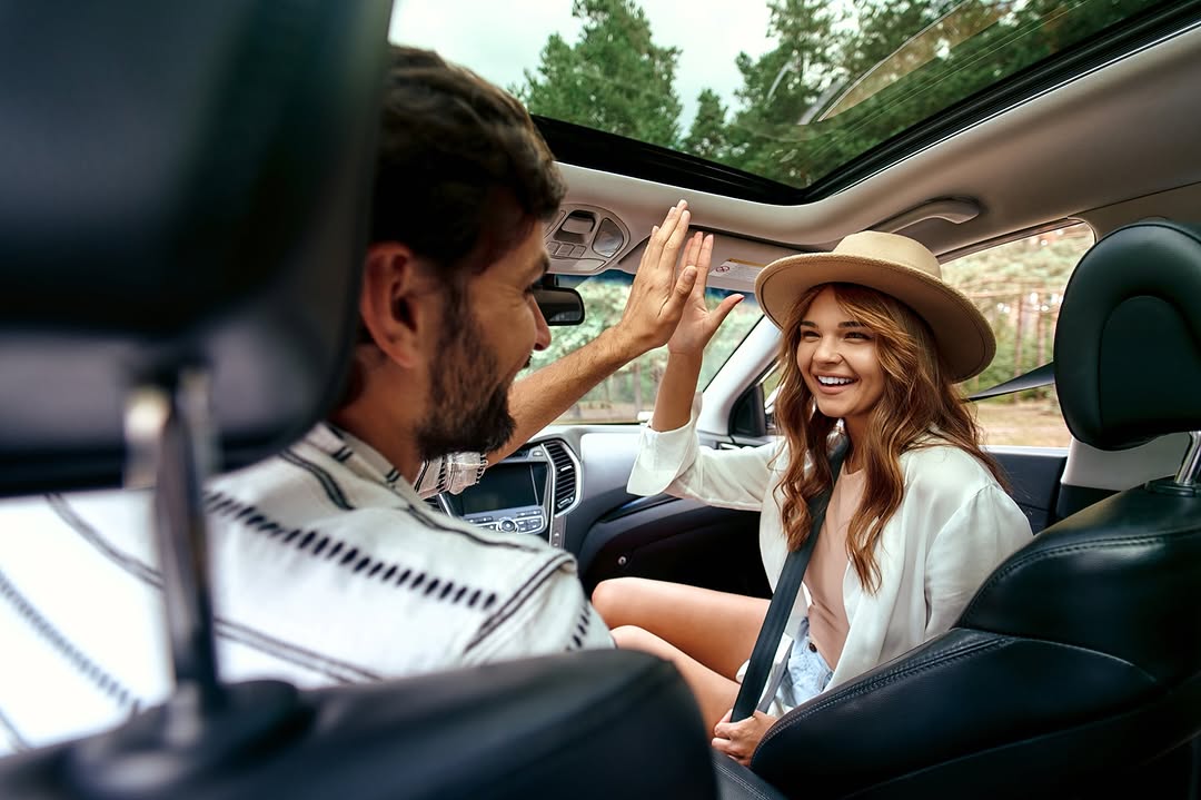 A happy couple enjoying a car journey, with the woman smiling and giving a high five to the man.