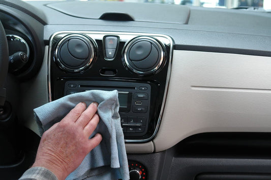 Hand drying a car dashboard with a microfiber cloth after washing the interior.