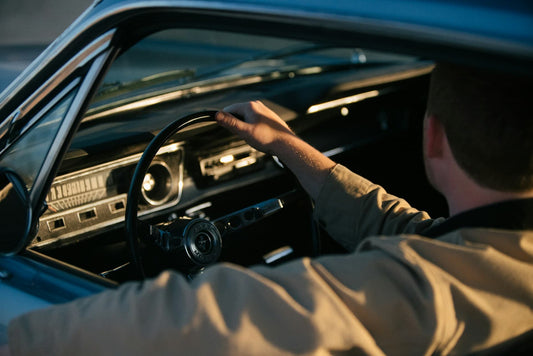 Man holding steering wheel while driving a vintage car during golden hour.