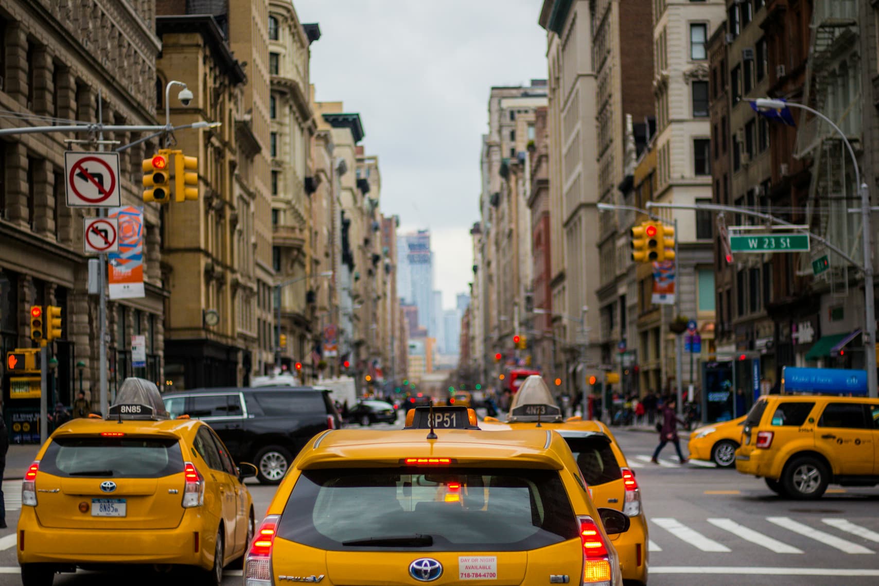 Yellow taxis driving down a busy street in New York City with tall buildings on both sides.