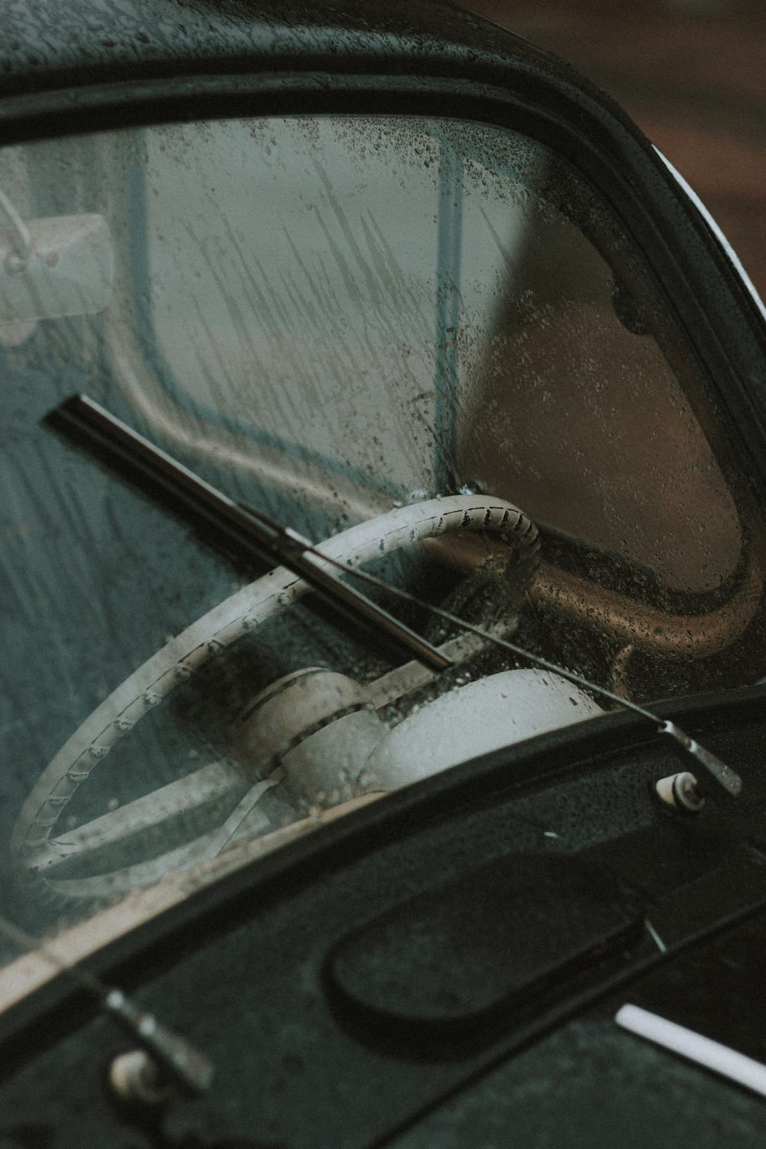 Vintage car steering wheel seen through a rain-soaked windshield.