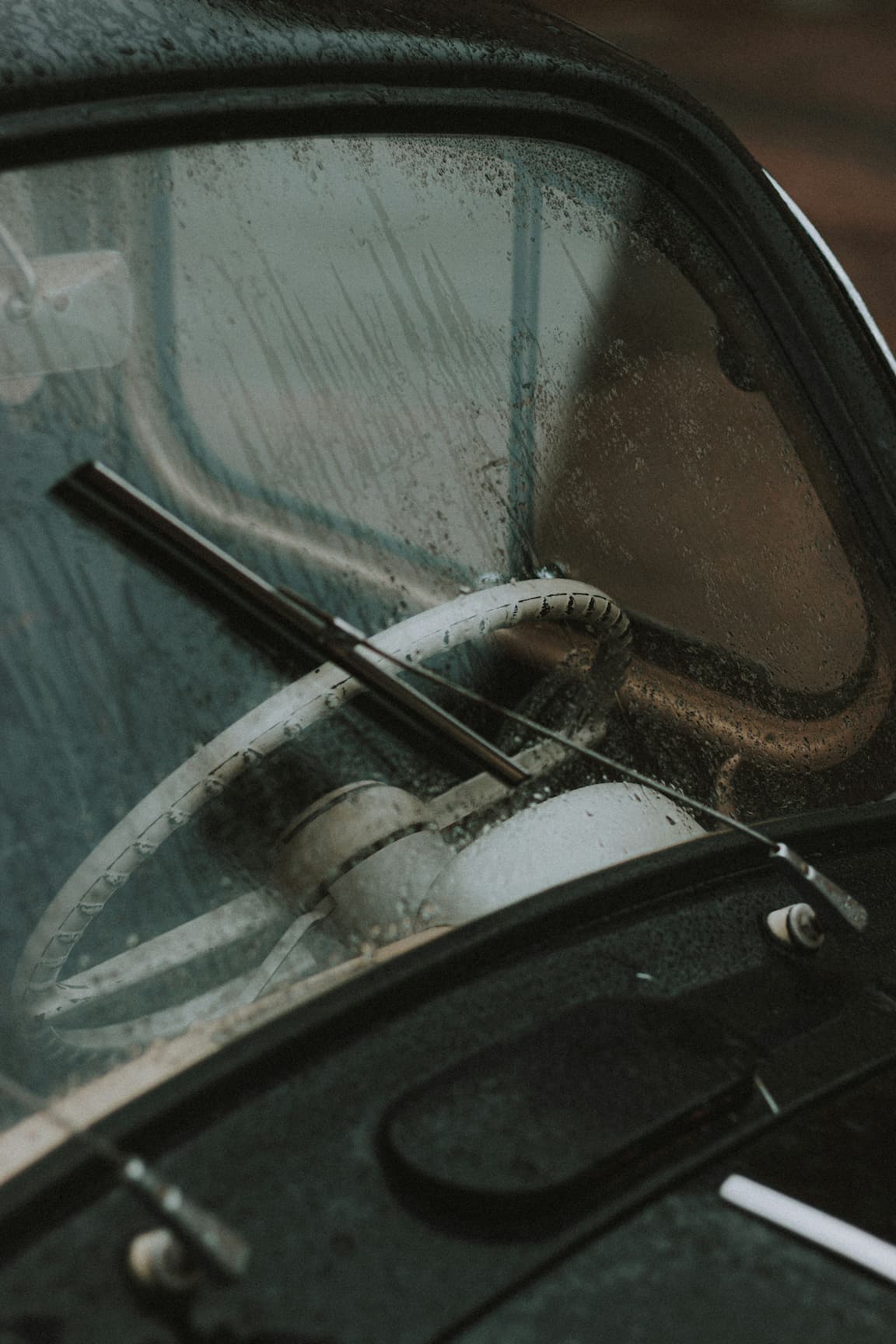 Vintage car steering wheel seen through a rain-soaked windshield.