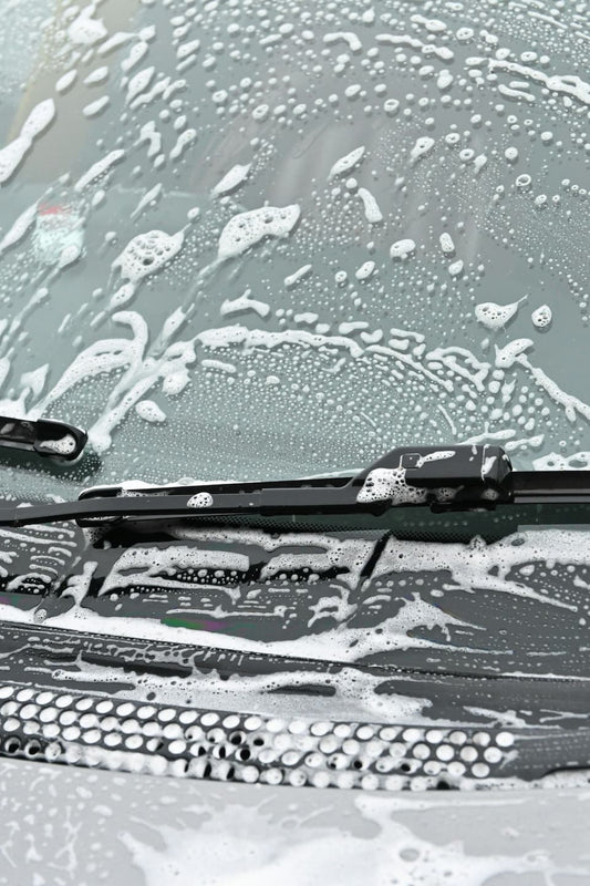 Washing a car windshield with soap to achieve a streak-free finish.