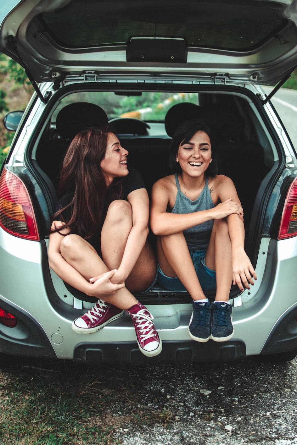 Two women sitting in the open trunk of a car, laughing and enjoying the moment.
