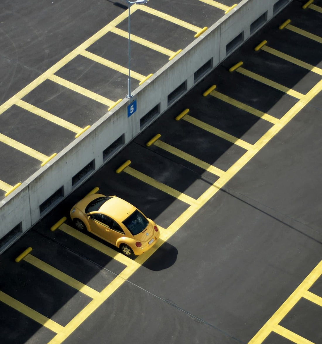 Yellow compact car parked alone in an empty, marked parking lot.