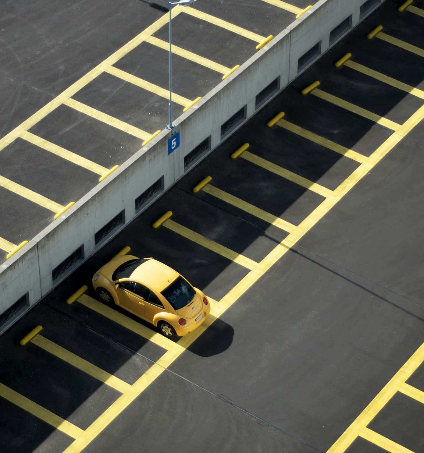 Yellow compact car parked alone in an empty, marked parking lot.