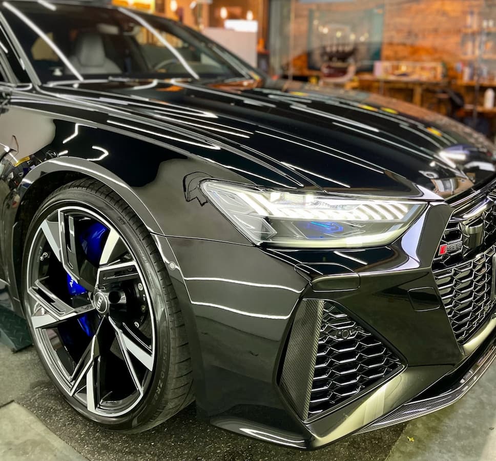 Close-up of a black sports car with polished body and alloy wheels in a detailing studio.