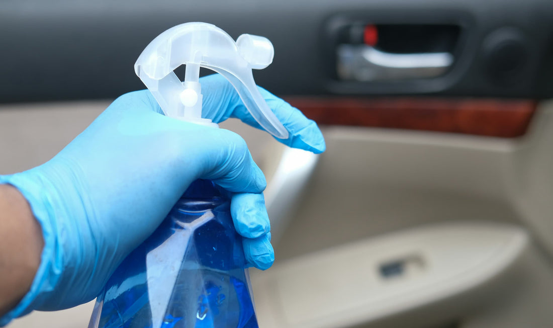 Cleaning car interior door panel using disinfectant spray and protective gloves.