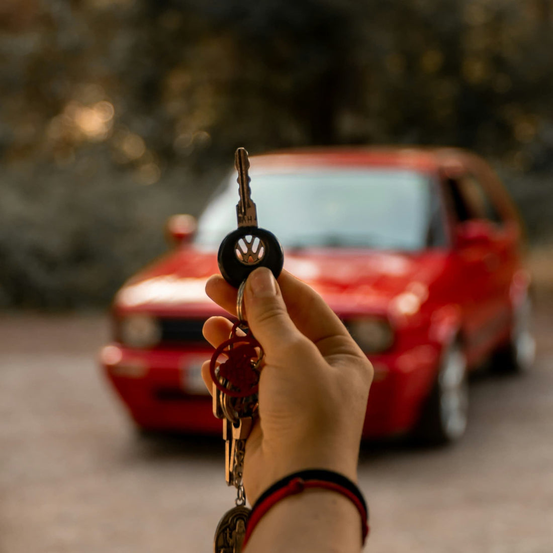 Person holding car key in front of parked red car outdoors.