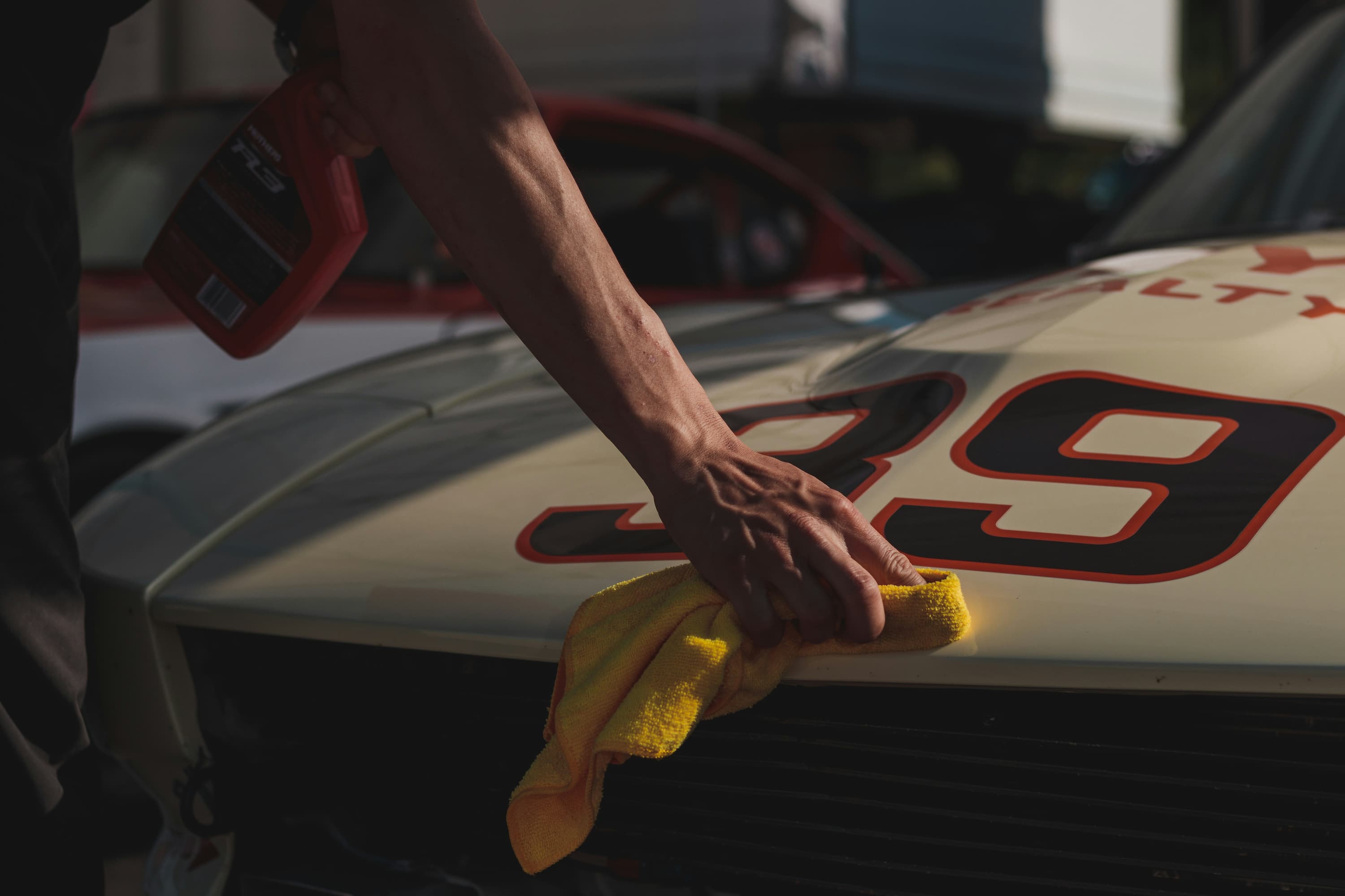 Hand polishing a racing car hood with yellow cloth and detailing spray