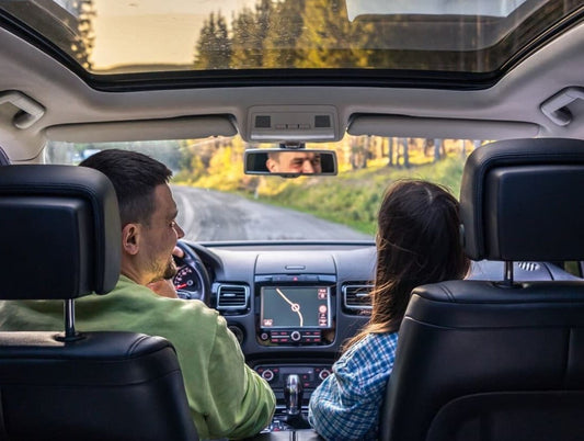 A couple enjoying a scenic road trip inside a modern car with an open sunroof.