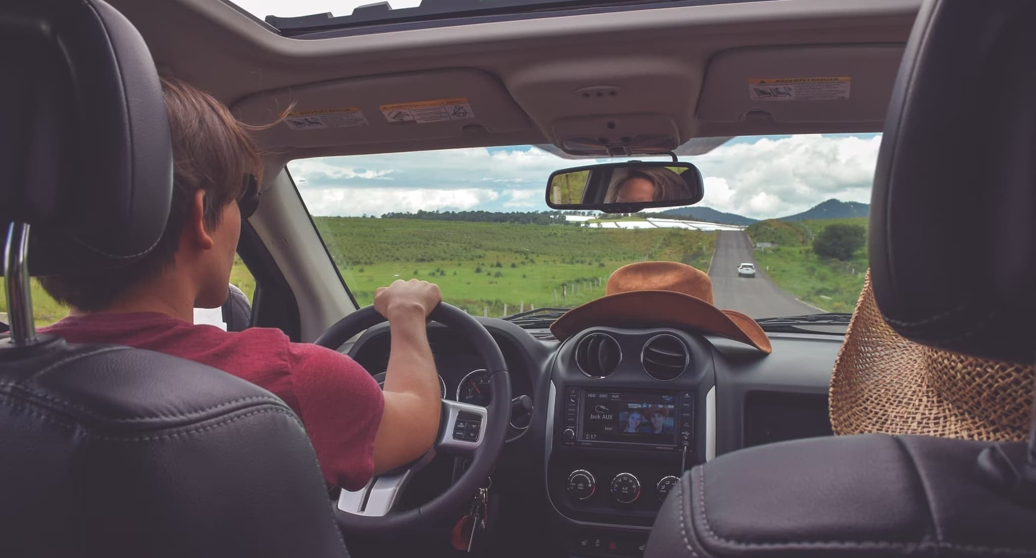 View from back seat showing driver on scenic road trip in a modern car interior with open roof.