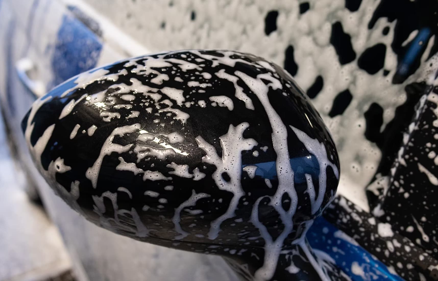 Car side mirror covered in foam during a thorough car wash.