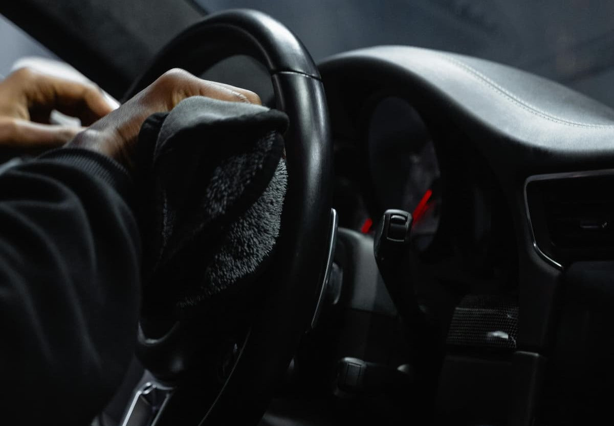 Cleaning car steering wheel with cloth inside vehicle interior for hygiene and maintenance.