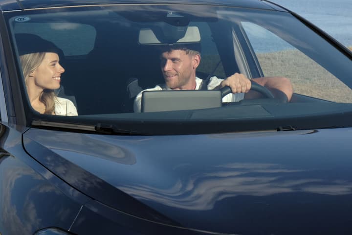 Smiling couple sitting inside a modern car, viewed from the front windshield.