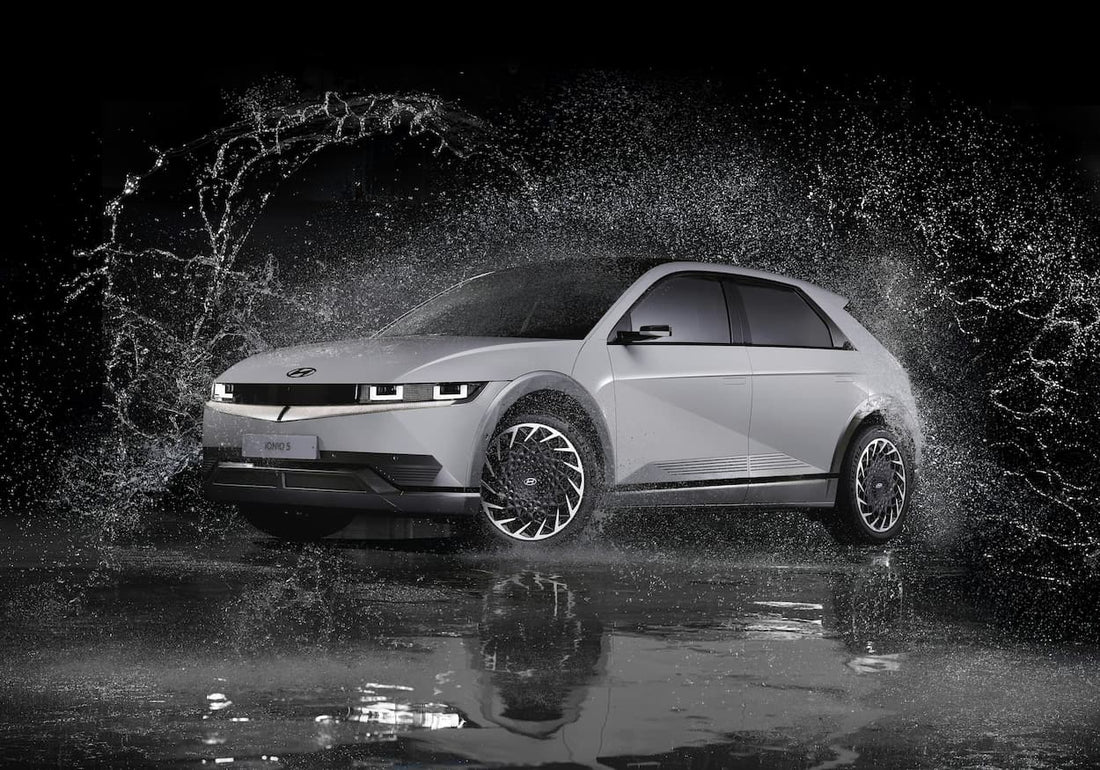 Electric car driving through a large water splash at night, showing dynamic motion and wet road surface.