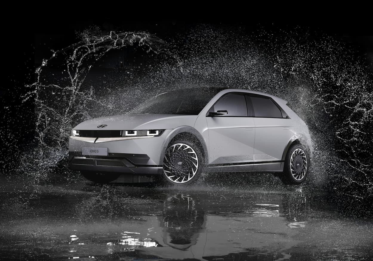 Electric car driving through a large water splash at night, showing dynamic motion and wet road surface.