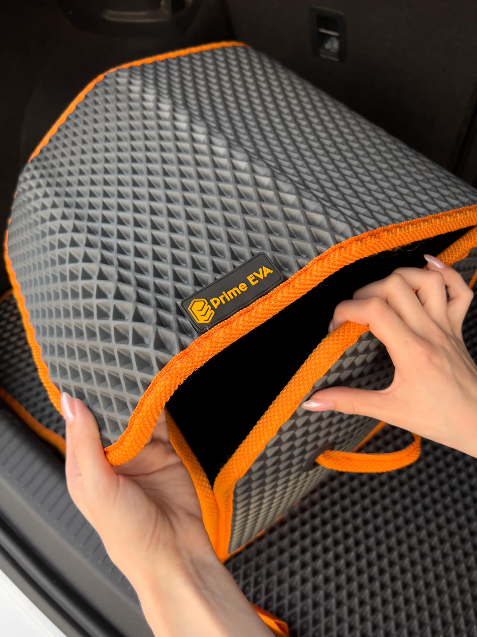 Hands holding a custom EVA car organizer bag with an orange border inside a car trunk.