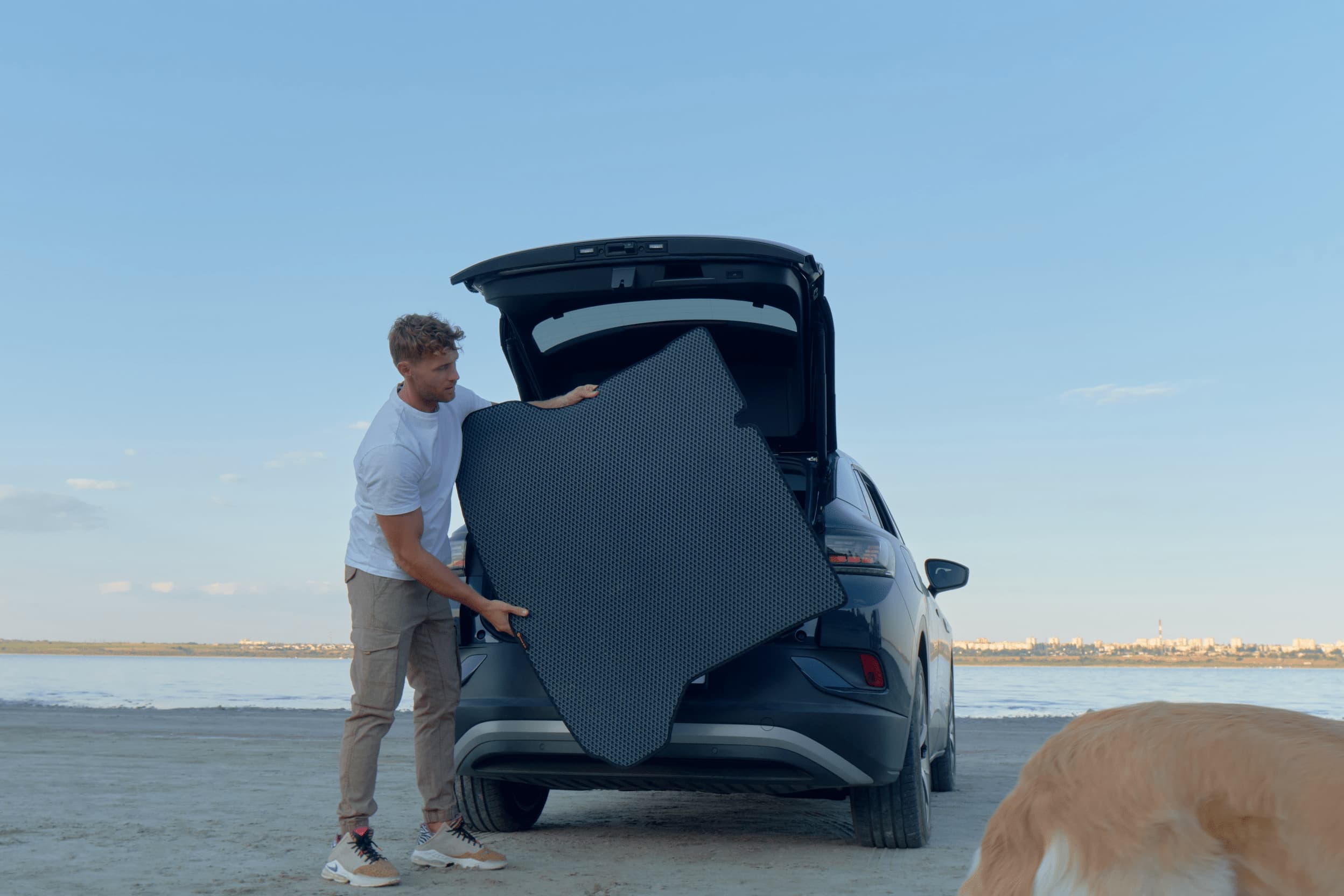 Man installing EVA trunk mat in car cargo area near beach showing custom fit protection.