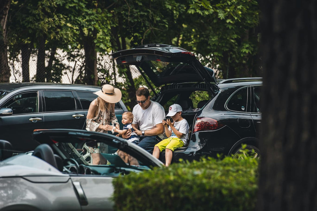 Family enjoying a picnic using the open car trunk as a seat during a road trip.