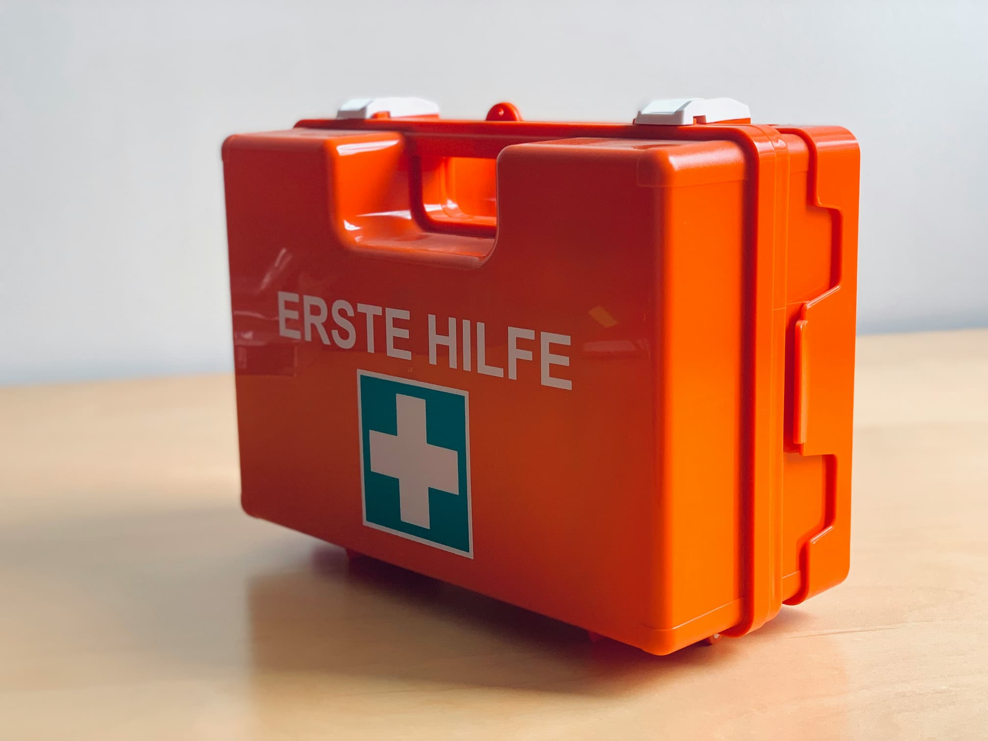 Orange first aid box labeled "Erste Hilfe" placed on a wooden table.