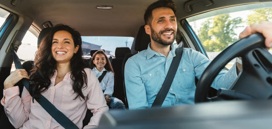 A happy family enjoying a road trip in their car, smiling and wearing seat belts.