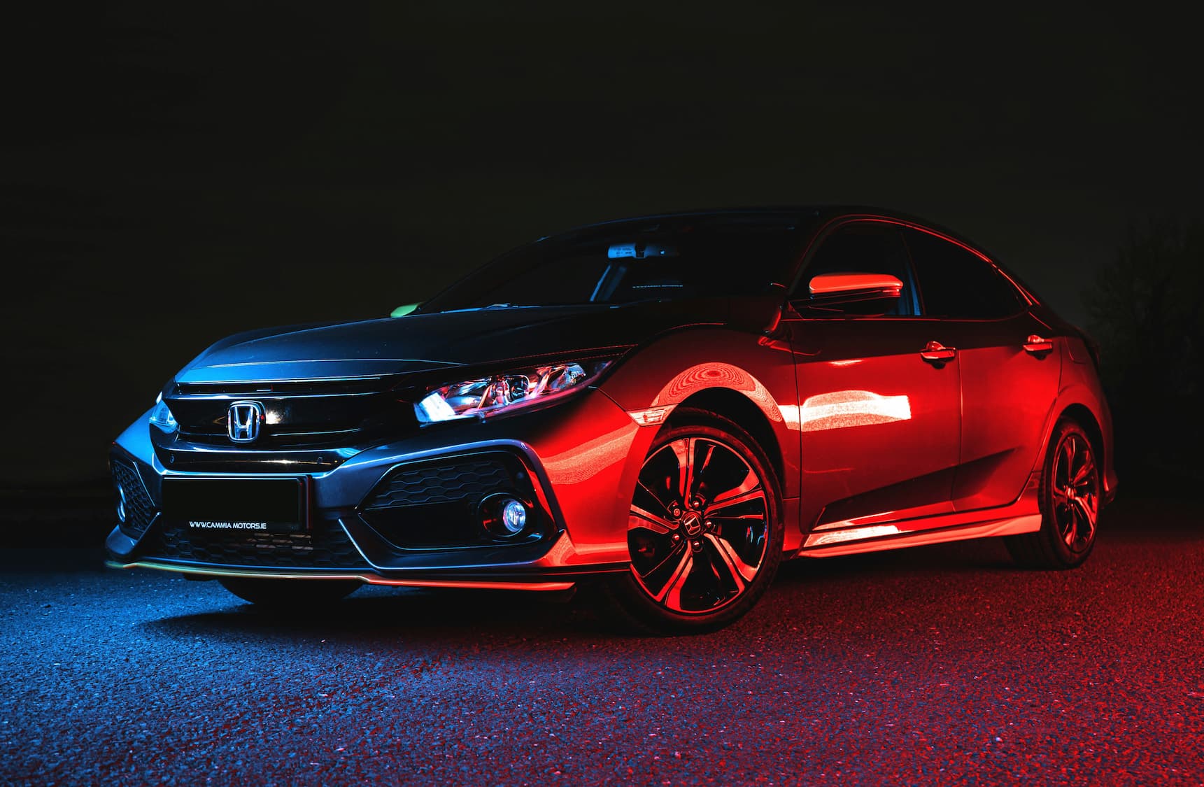 Honda Civic parked at night with dramatic red and blue lighting highlighting sporty exterior design.