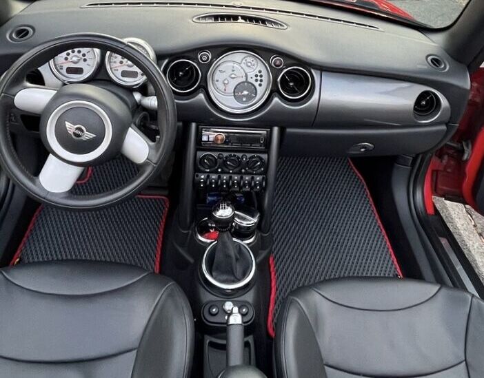 Mini Cooper interior with custom black floor mats featuring red trim.