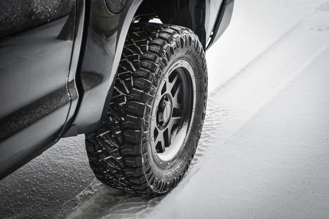 Off-road car tire with deep tread creating strong grip while driving on snowy winter road.
