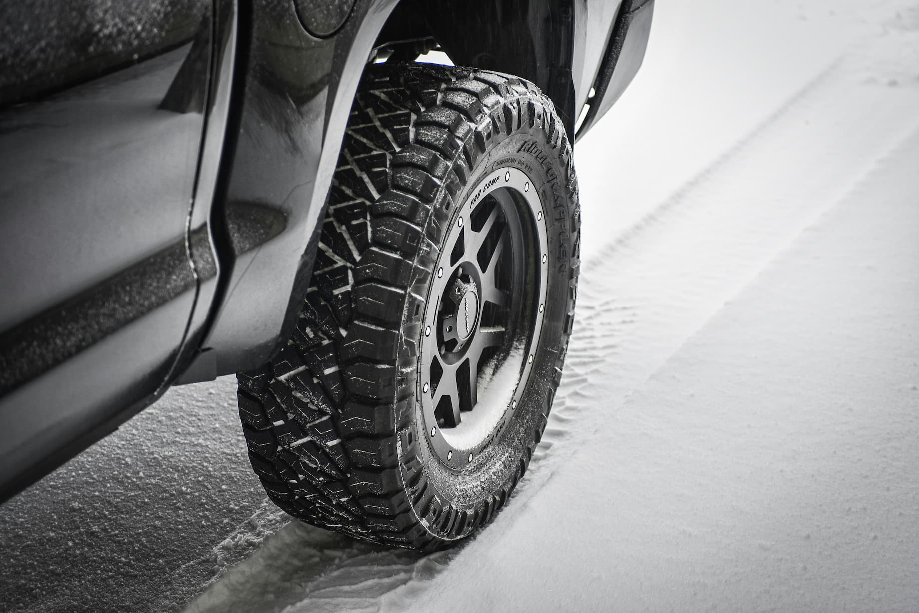 Off-road car tire with deep tread creating strong grip while driving on snowy winter road.