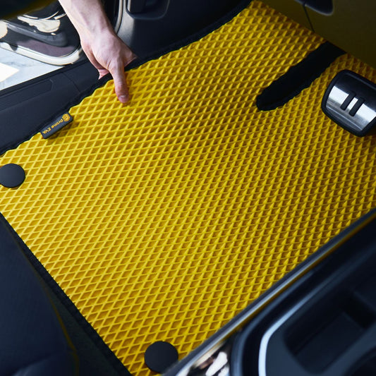 Hand installing a yellow Prime EVA car floor mat with textured diamond-shaped surface in a car interior.