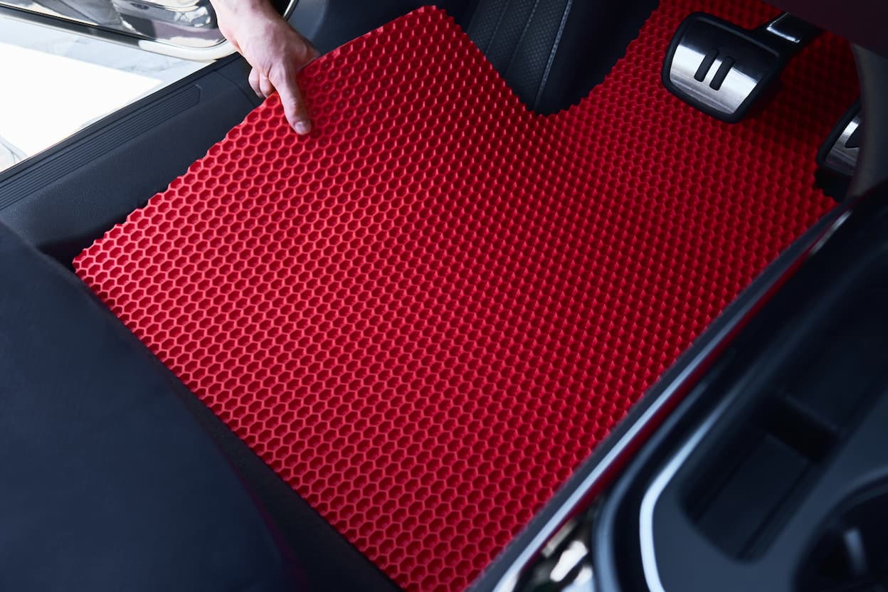 Red EVA car floor mat being installed inside the vehicle near the driver's pedals.