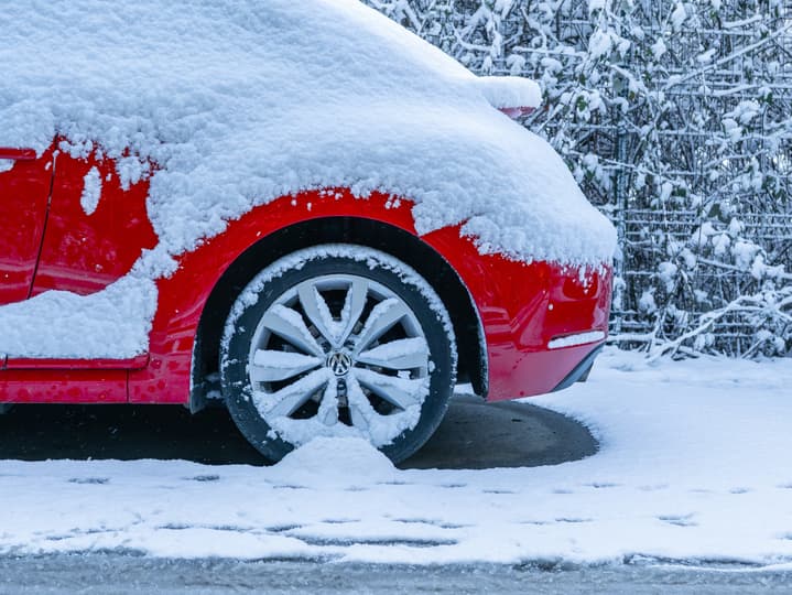 Red car covered in snow with a snowy rear wheel and parked on a winter road.
