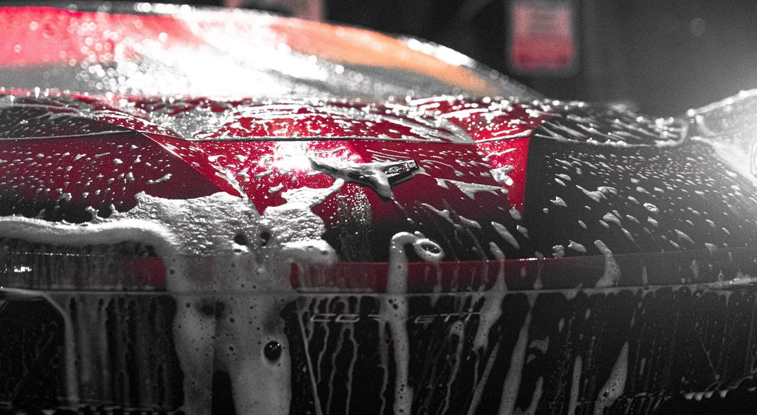 A red car covered in foam during a car wash, highlighting the soap suds and cleaning process.