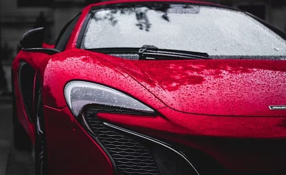 Close-up of a red sports car covered in raindrops, highlighting its sleek design.