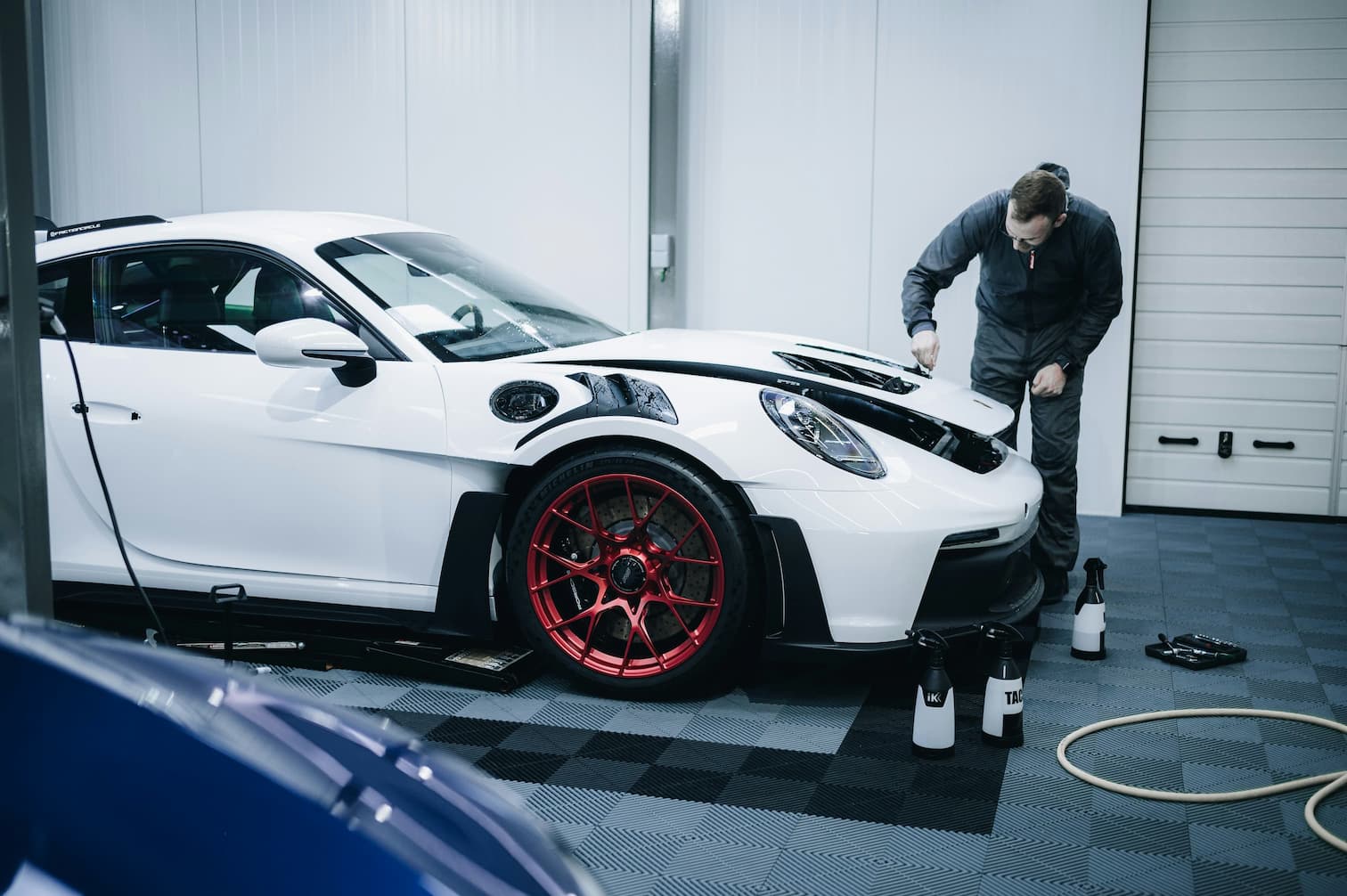 Car detailing specialist inspecting a white sports car in a professional garage environment.