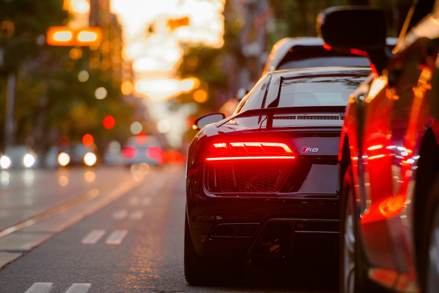 Close-up of a black sports car on city street during sunset with brake lights on.