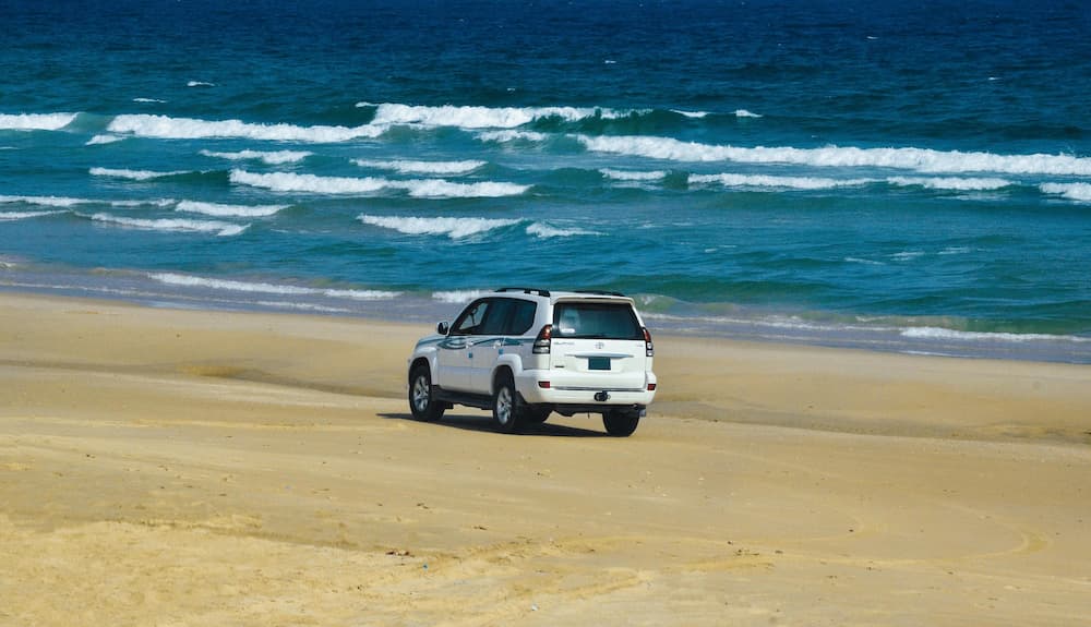 SUV driving along sandy beach near ocean highlighting outdoor travel and adventure lifestyle.