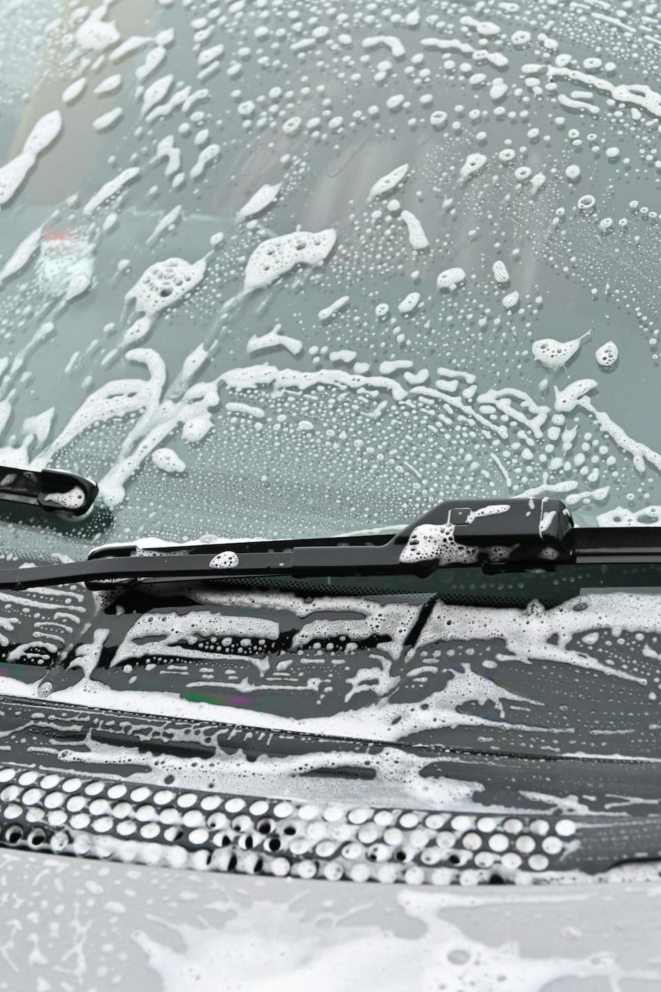 Washing a car windshield with soap to achieve a streak-free finish.