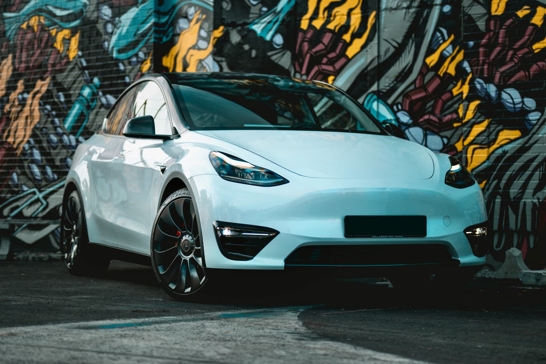 White Tesla electric car parked in an urban area in front of a colorful graffiti wall.