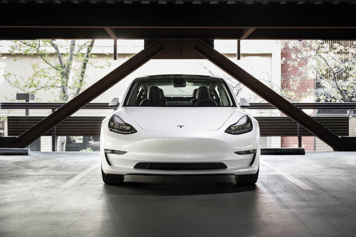 White Tesla electric car parked in a modern parking garage, front view with clean minimalist design.