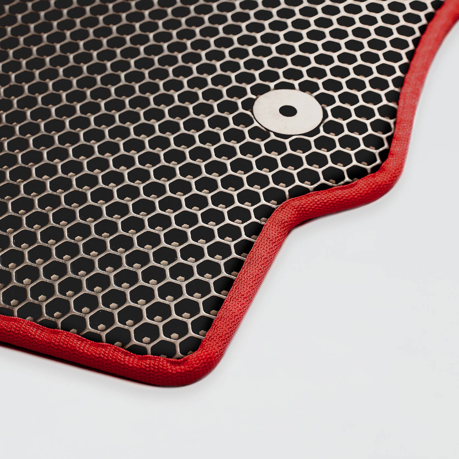 Close-up of a black honeycomb mat with a red border and a metal button.