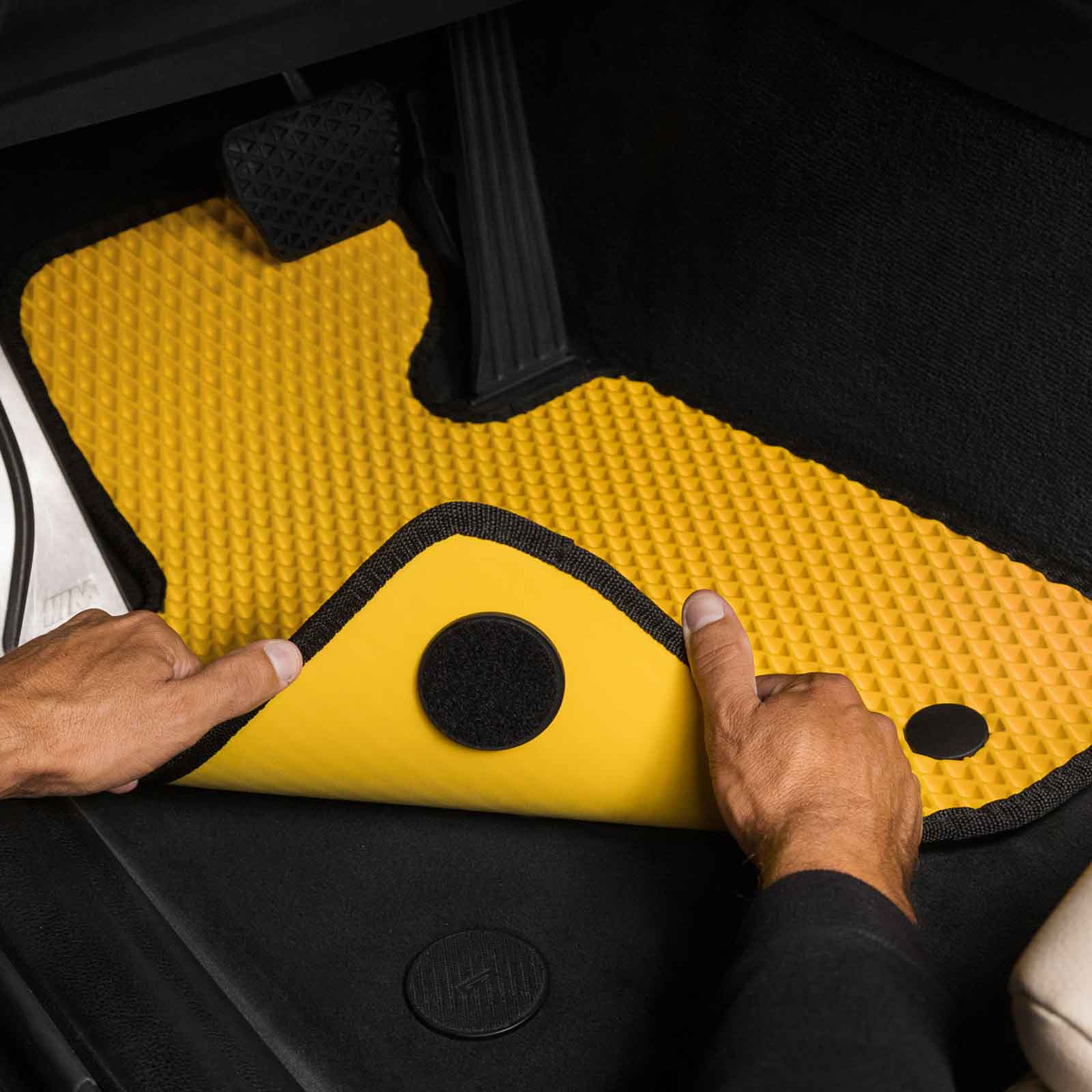 Close-up of a custom yellow car floor mat being installed in a BMW vehicle.