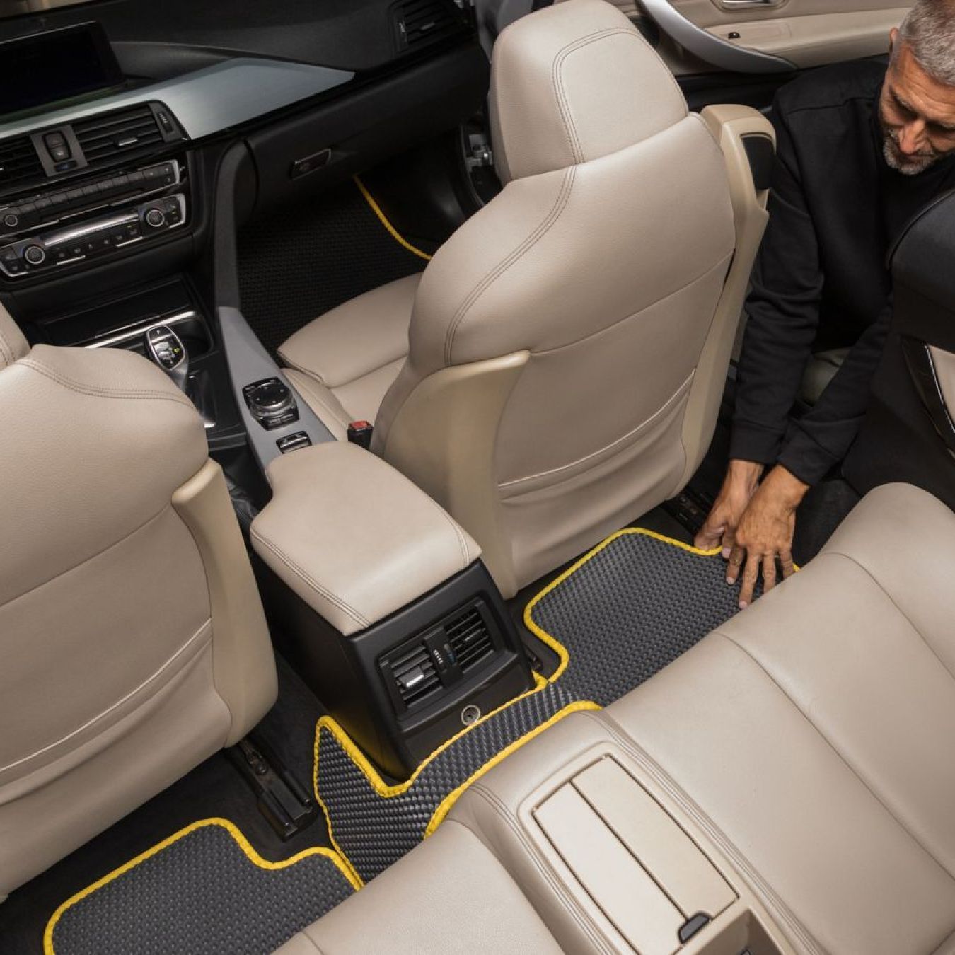 Grey and yellow rear seat floor mats being installed in a BMW luxury sedan.