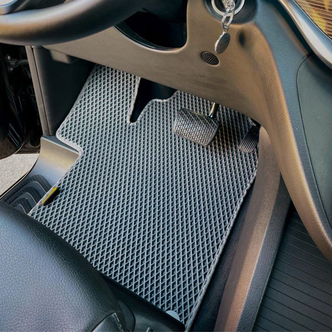 Close-up of a custom grey car floor mat installed in a car interior.