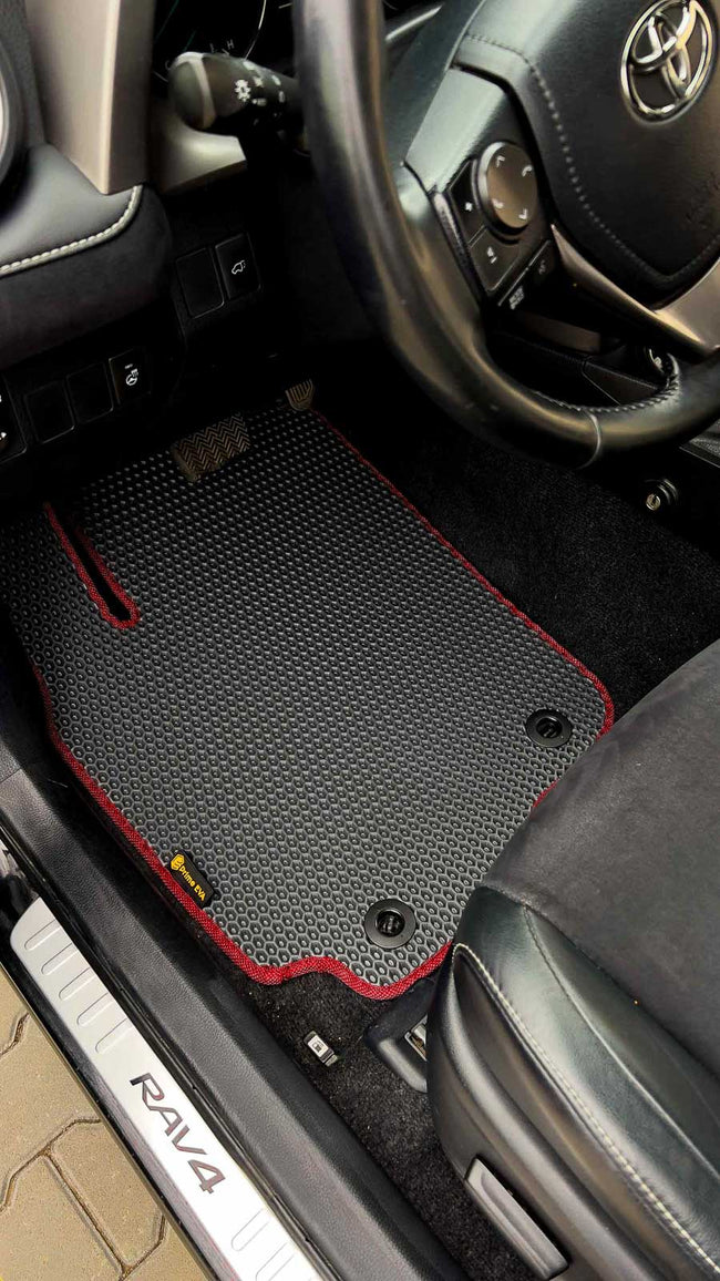 Close-up of a custom black car floor mat with red stitching in a Toyota RAV4 interior.