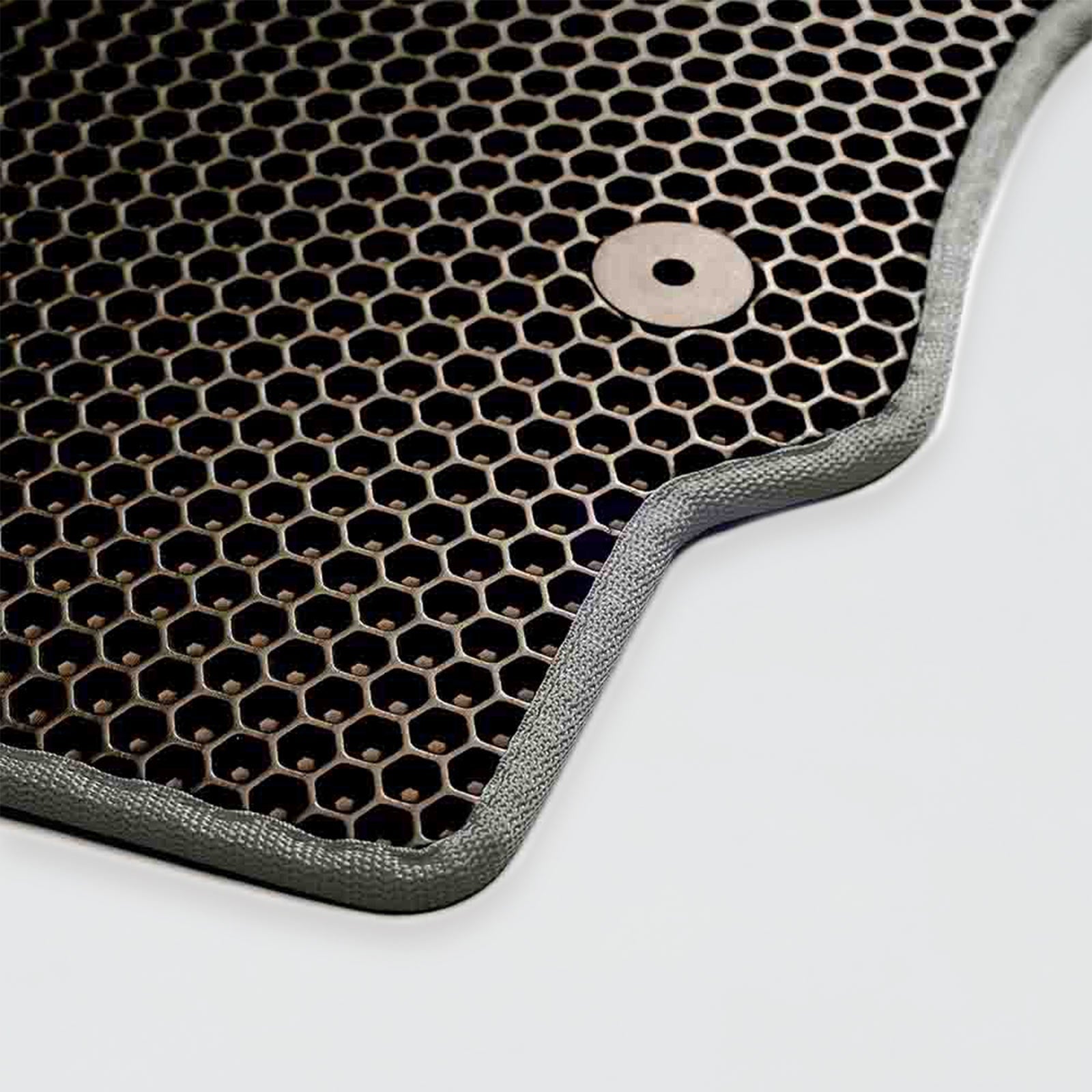 Close-up of a textured black hexagonal car mat with a circular fastener.