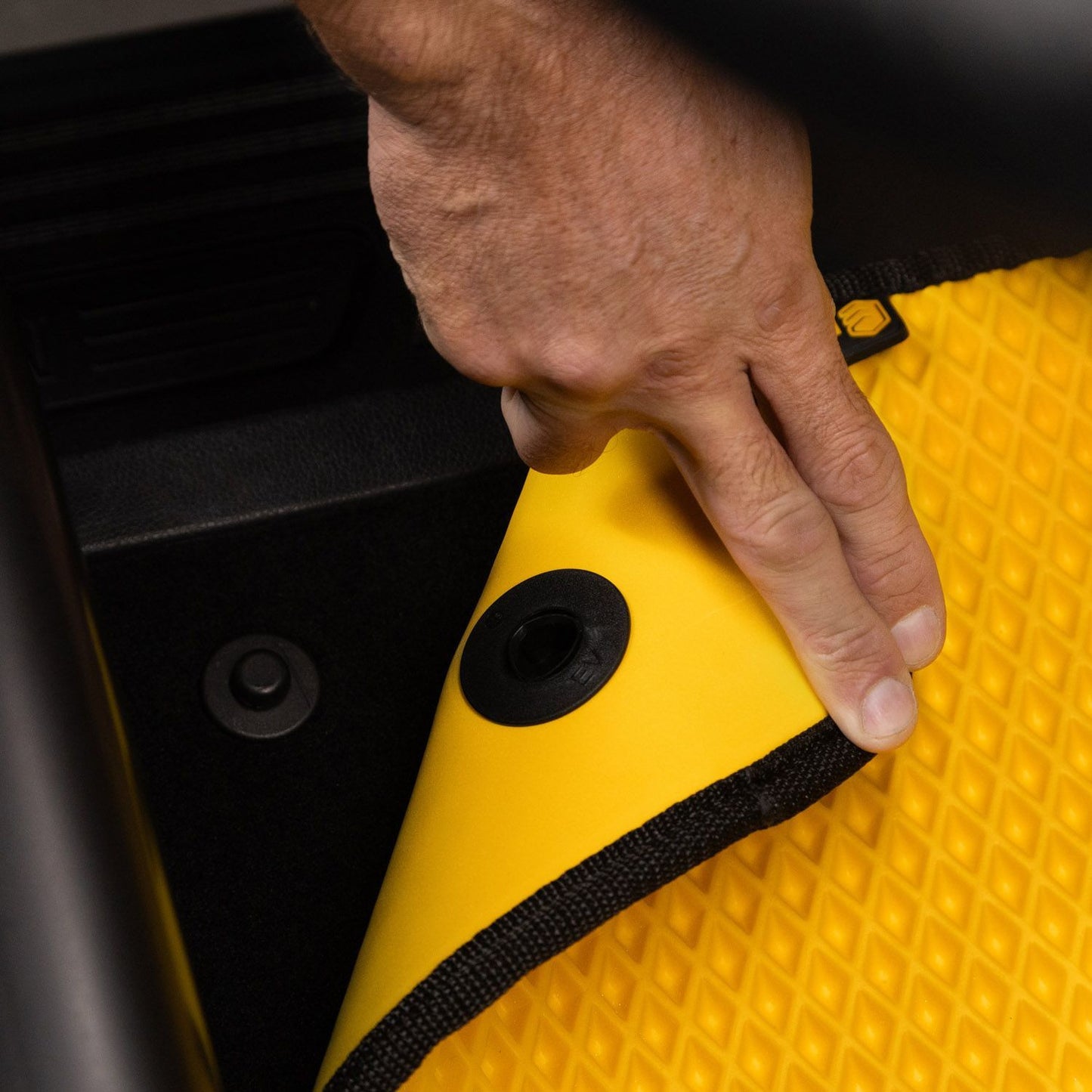 Close-up of a yellow floor mat being installed in a van with secure fasteners.